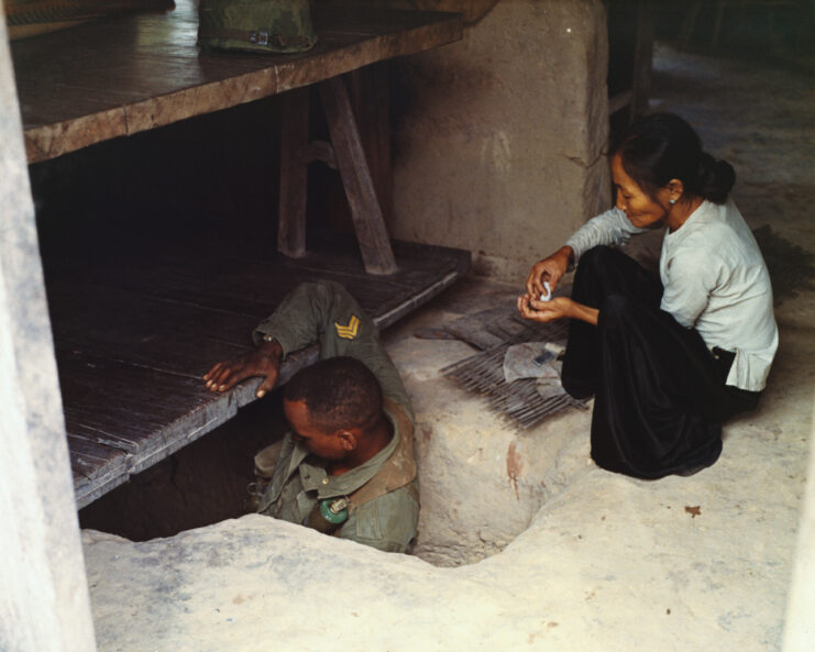 US soldier entering a tunnel while a woman watches nearby.