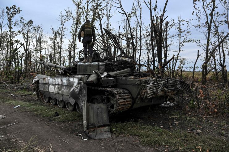 Ukrainian soldier standing on top of a destroyed Russian tank.