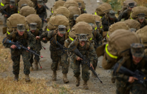 US Marine Corps recruits running with large rucksacks on their backs