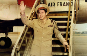 Audie Murphy, America's "most decorated soldier", waves to crowds while descending the steps of an Air France plane.