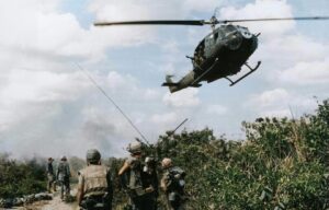 Soldiers of the fourth U.S. Marine Regiment patrol the demilitarized zone in Vietnam as a Marine Corps "Huey" helicopter passes overhead, Vietnam War, 1967.