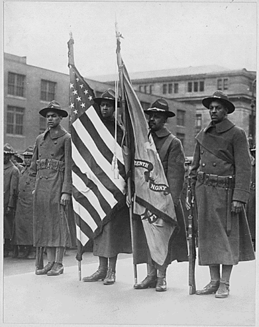 Members of the 15th New York National Guard Regiment standing with their regimental flag and the American flag