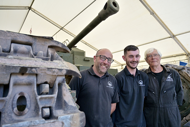 Three members of the Tank Museum staff standing next to a Churchill Mark III tank