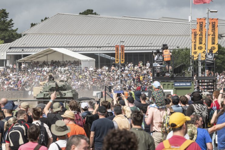 Crowd watching a tank drive around a dirt track