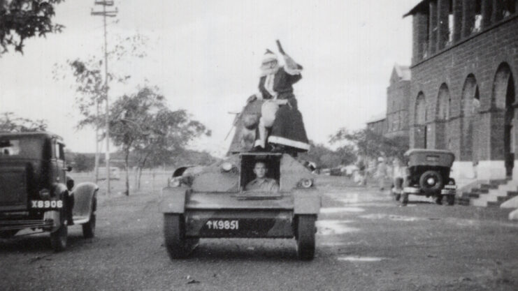 A man dressed as Santa Claus sitting on the main gun of a tank that's driving down a street