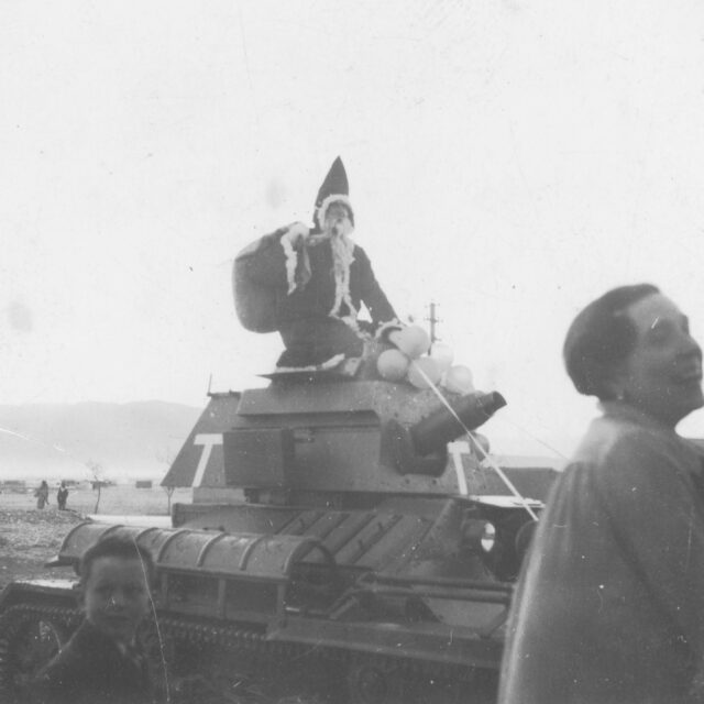 Man dressed as Santa Claus sitting atop a tank, with a woman standing nearby