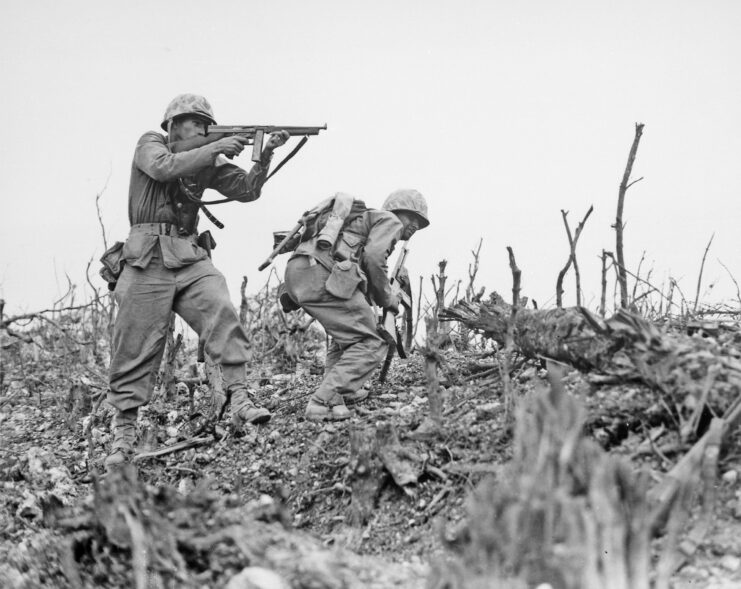 Two members of the 1st Marine Regiment walking through rubble and downed trees