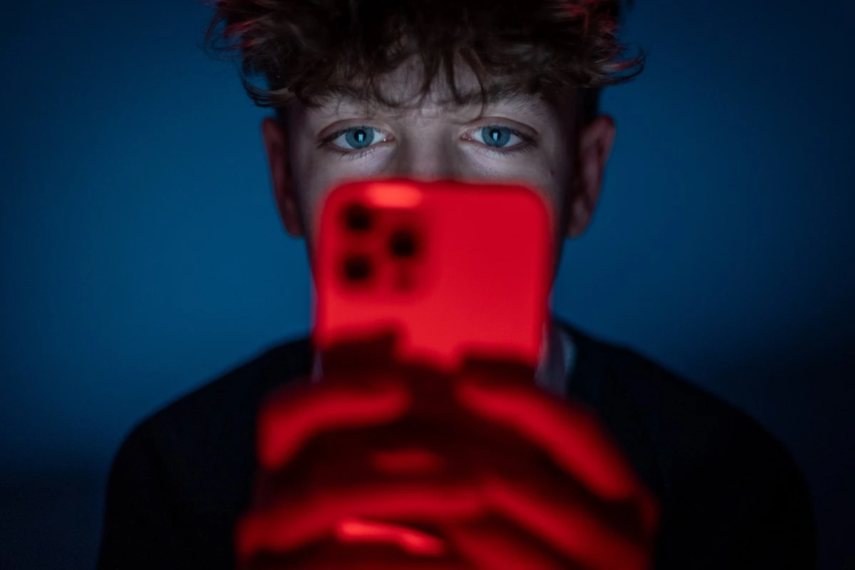 An image of a man looking at his iphone in his dimly lit room.