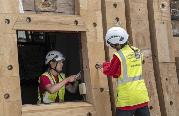 Two shipwrights working on large timbers