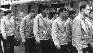 Prisoners lined up for release on 27 March 1973 at the airport. Marines pictured among the 27 returnees freed that day were Sgt Jose J. Anzaldua, fourth from the left, and Sgt Dennis A. Tellier, second from the right. The bus was camouflaged as a defense against air attack.