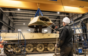 Construction worker lifting the turret off King Tiger V2 with a rope, while other workers watch from behind the tank
