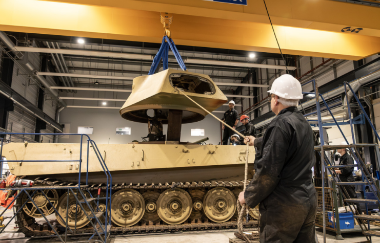 Construction worker lifting the turret off King Tiger V2 with a rope, while other workers watch from behind the tank
