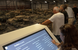 Visitors looking over a balcony into a workshop filled with military tanks